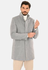 Cappotto grigio in lana con colletto alto, chiusura con un solo bottone e tasche laterali. Presenta un design essenziale e tessuto strutturato.