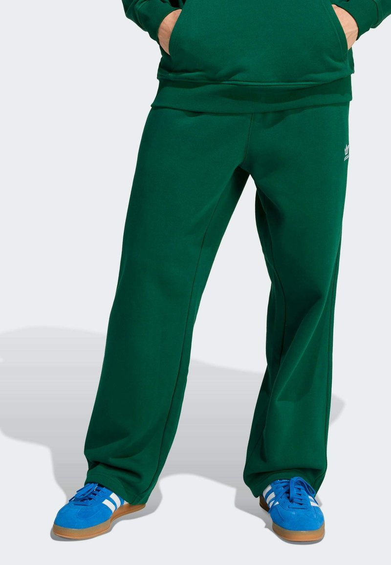 Zielone dresy z miękkiego materiału, w luźnym kroju, z bocznymi kieszeniami i małym logo na lewym udzie, połączone z niebieskimi butami.