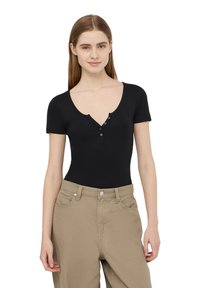 Body nero a maniche corte con scollo a V profondo, abbellito da una placca con tre bottoni e materiale in cotone elasticizzato, abbinato a pantaloni kaki chiari.