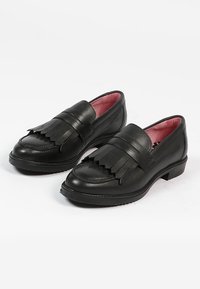 Zwarte leren loafers hebben een platte hak, decoratieve franjes aan de voorkant en een roze binnenvoering. Gladde textuur met gestikte accenten.