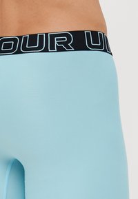 Helle blaue Sportleggings mit einer enganliegendem Design, versehen mit einem schwarzen Bund, auf dem "OUR" steht. Der Stoff ist glatt und dehnbar.