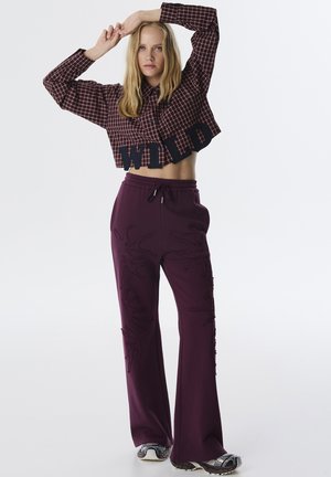 Korte gebloemde blouse met de applicatie "WILD", gecombineerd met bordeauxrode brede broek met textuurpatronen en een strikband.