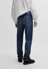 Jeans in denim blu scuro con taglio dritto, caratterizzati da un design della tasca posteriore e un patch blu con il logo HUGO sulla vita.