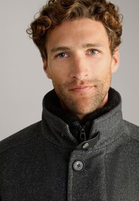 Grau gemischter Wollmantel mit hohem Kragen, Reißverschluss und Knopfdetails. Mit strukturiertem Muster und kontrastierender Innenausstattung.