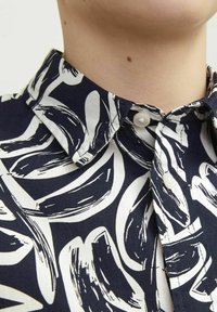 Camicia di cotone blu navy con un motivo astratto bianco, caratterizzata da un colletto, chiusura con bottoni e una texture liscia.