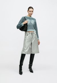 Ανοιχτό μπλε πλεκτό πουλόβερ με σχέδιο καρδιάς, ασημένιοι μεταλλικοί σορτς και μαύρες μπότες που φτάνουν μέχρι το γόνατο. Μαύρη τσάντα με κυκλικό μεταλλικό στοιχείο.