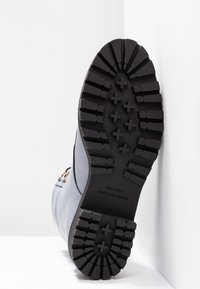 Semelle de botte en caoutchouc noir avec des rainures profondes et des motifs en forme de croix, affichant le nom de la marque et le texte "Fabriqué en Espagne" sur fond blanc.