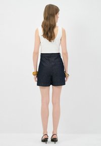 Mörka denimshorts med en skräddarsydd passform, som har bakfickor och en slät midja, matchat med en figurnära vit linne.