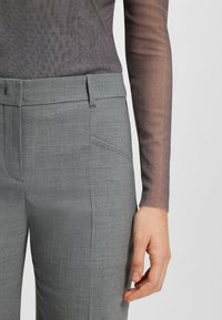 Grau maßgeschneiderte Hosen aus einem strukturierten Stoff, mit flachem Frontschnitt, seitlichen Taschen und slim fit, kombiniert mit einem transparenten Langarmtop.