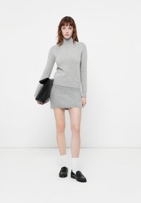 Siv rokovni pulover s turtleneck iz pletenine, ki se ujema s kratko krilo, ki ima mehak tekstur. Model drži črno torbico, nosi temne loafers in bele nogavice.