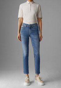 Polo shirt léger à rayures avec des manches courtes, associé à un jean en denim bleu à jambe droite et des baskets beiges épaisses.