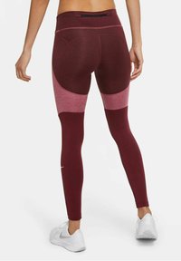 Burgundy-idrottsleggings med en åtsittande design, kontrasterande paneler i ljusare nyanser och en blixtlåsförsedd bakficka för förvaring.