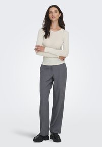 Top crema de manga larga con tejido acanalado, combinado con pantalones grises a rayas y zapatos negros gruesos. Diseño sencillo con silueta ajustada y textura suave.