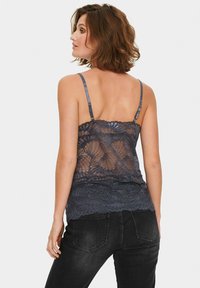 Tamsiai mėlynas nėriniuotas camisole su reguliuojamomis petnešomis, dekoruotas gėlėmis ir banguotu scallop apdaila, derinamas su juodais džinsais. Medžiaga permatoma ir minkšta.