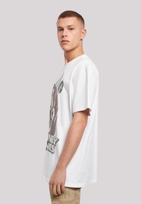 Bílý bavlněný tričko s velkým grafickým potiskem karikatury na přední straně. Volný střih a krátké rukávy.