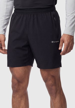 Man draagt zwarte Champion sportshorts met ritssluiting zak en geperforeerde details op de benen, weergegeven van taille tot knieën.