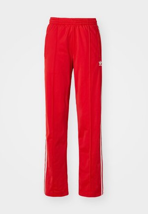 Pantalons de jogging rouges avec un waistband élastique, des poches latérales, et des bandes blanches sur les côtés. Fabriqués en tissu léger et lisse. Présentent des détails de logo.