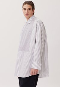 Camicia bianca con sottili righe verticali, maniche lunghe e colletto a bottoni. Presenta una vestibilità ampia e un orlo curvo.