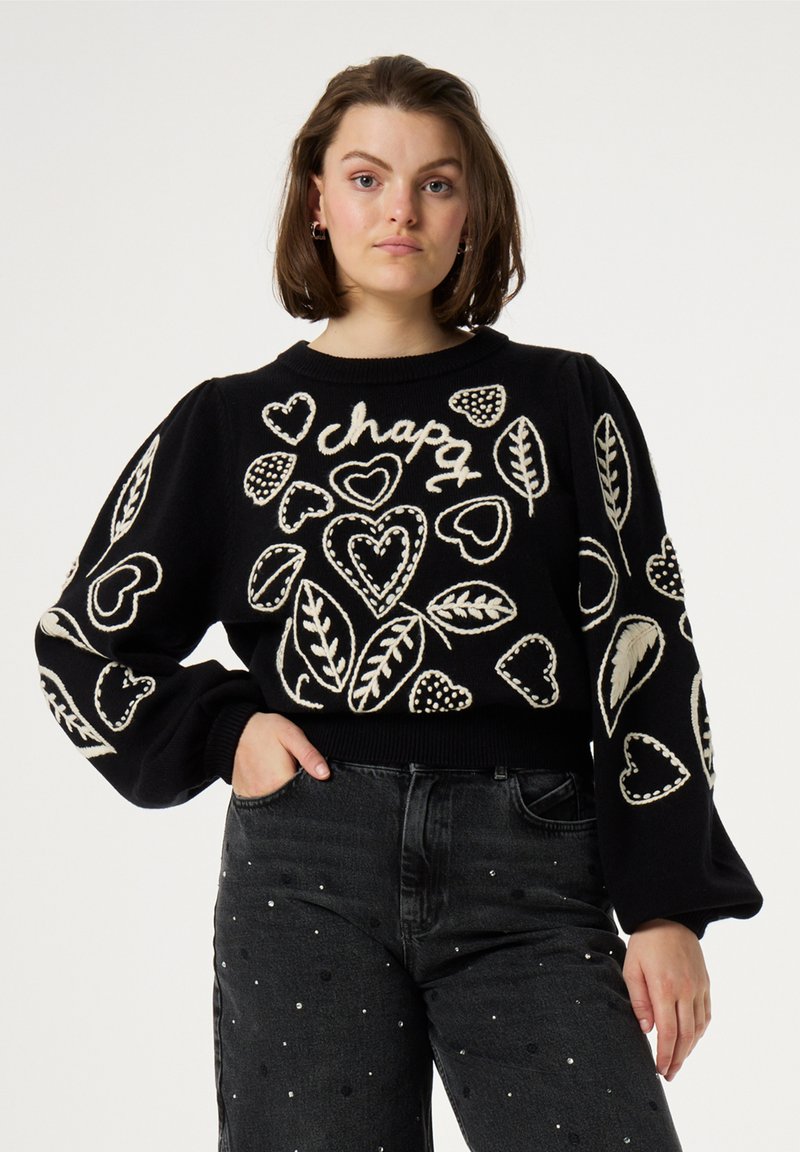 Zwarte trui met witte geborduurde harten en bladeren, ronde halslijn en puffed lange mouwen. Gekocht met hoge taille donkere jeans.