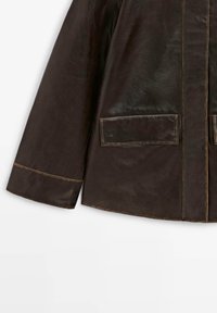 Veste en cuir marron avec une texture lisse, deux poches avant et des surpiqûres contrastantes le long des bords et des coutures.