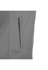 Grijze stof met een gladde textuur, voorzien van een verticale, verborgen zak aan de linkerkant. Het ontwerp is minimalistisch en functioneel.