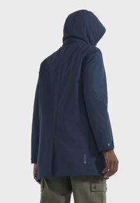 Mornarice plava Gore-Tex jakna s kapuljačom, ravnog kroja, s gumbima na rukavima i glatkom, mat finišu s minimalnim dizajnerskim elementima.