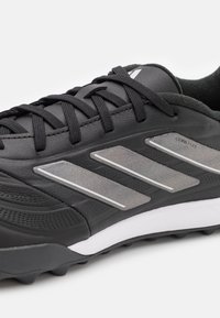 Scarpa da ginnastica nera con tomaia sintetica, motivi testurizzati, dettagli argentati e una suola intermedia bianca. Presenta lacci standard e tacchetti stampati.