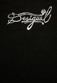 Srebrny metaliczny napis "Desigual" z dekoracyjnymi kropkami i małym kwiatkiem na czarnym tle materiału.