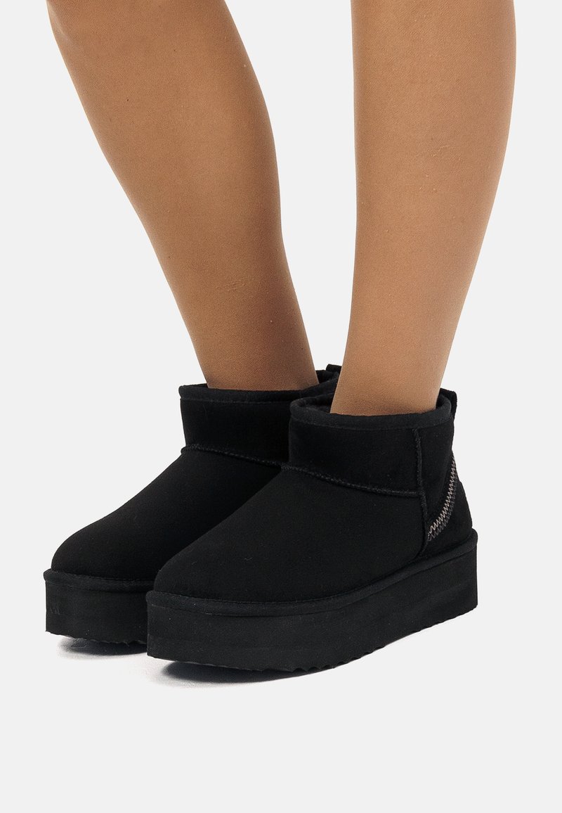 Stivali alla caviglia in suede nero con suola piatta in gomma. Presentano una manica piegata e cuciture testurizzate sul lato per il dettaglio.