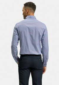 Långärmad skjorta i ljusblått med ett geometriskt mönster, i kombination med svarta byxor. Skjortan har knäveck och en klassisk kragsdesign.