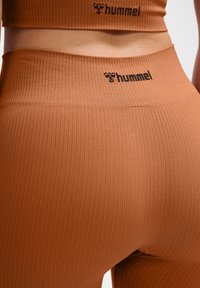 Rippenbraune Leggings mit hoher Taille und schwarzem "hummel"-Logo am Bund. Der Stoff hat eine glatte, dehnbare Textur.