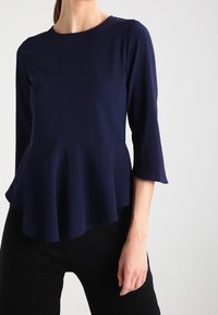 Top peplum blu navy con maniche tre quarti, realizzato in tessuto leggero. Presenta un collo rotondo e un orlo svasato per un aspetto strutturato.