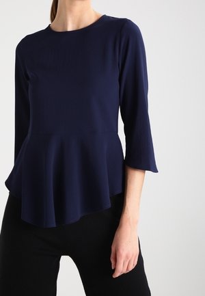 Top peplum blu navy con maniche tre quarti, realizzato in tessuto leggero. Presenta un collo rotondo e un orlo svasato per un aspetto strutturato.