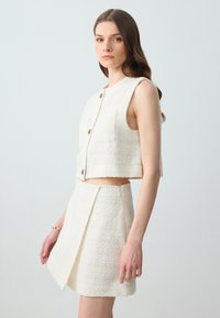Witte, gestructureerde twee-delige set met een cropped vest met knoopsluiting en een bijpassende asymmetrische rok met een ritssluiting aan de zijkant.
