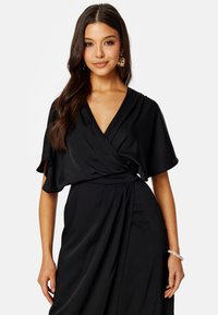 Vestito avvolgente nero realizzato in tessuto liscio. Presenta maniche corte e ampie e un profondo scollo a V. Il design avvolgente accentua la vita. Semplice ed elegante.