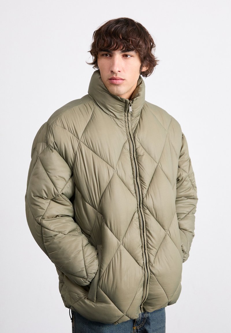 Olive green puffer jacket with a diamond quilt pattern, high collar, and front zipper. Features a relaxed fit and side pockets.