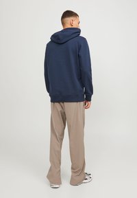 Sudadera azul marino con bolsillo tipo canguro frontal y capucha ajustable con cordón, combinada con pantalones de pierna ancha de un ligero tono beige.