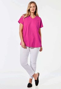 Helles pinkes V-Ausschnitt-T-Shirt, kurze Ärmel, kombiniert mit weißen Slim-Fit-Hosen und schwarzen Slippern. Glatte Stofftextur, lässige Passform.