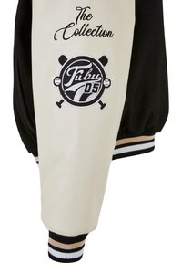 Čierna a krémová bomber bunda so vyšívaným textom "The Collection" a kruhovým logom s nápisom "Tubu 05," doplnená pruhovanými manžetami.