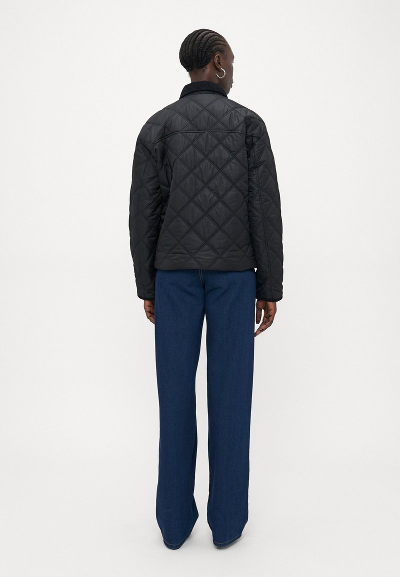 Veste noire matelassée avec un motif en diamant, dotée d'un col et de manches longues, accompagnée de pantalons en denim bleu à jambes larges.