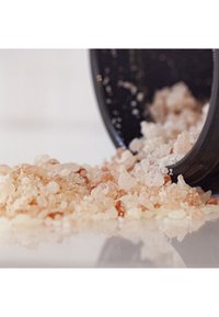 Des cristaux de sel rose et blanc se déversent d'un récipient noir, mettant en évidence des formes irrégulières et une texture grossière sur une surface réfléchissante.