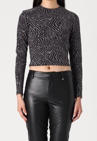 Musta ja hopeinen pitkähihainen paita, jossa on seepranraita-kuvio, valmistettu teksturoidusta, joustavasta kankaasta; lyhyempi malli paljastaa vatsan.