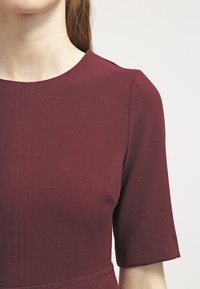 Vestido corto burdeos de manga corta, con un escote redondo y detalles de costura vertical, en una tela suave y texturizada.