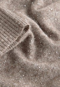 Light brown knit fabric with a soft texture, featuring scattered shiny sequins and ribbed detailing along the edge.