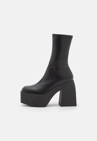Zwarte platformlaarzen met een vormpastende bovenkant en een chunky rechthoekige hak. Glad leer met minimale stikseldetails.