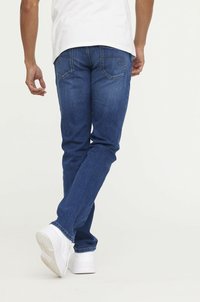 Jean bleu en denim avec une coupe droite, poches arrière ornées de coutures, assortis avec des chaussures de sport blanches.