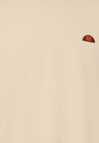 T-shirt in cotone beige con maniche corte, caratterizzato da un piccolo design ricamato in arancione e nero sulla parte sinistra del petto.