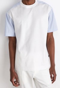 Lyhythihainen paita, jossa on valkoinen etuosa ja siniraidalliset hihat. Valmistettu pehmeästä kankaasta, jossa on pyöreä pääntie ja rento istuvuus.