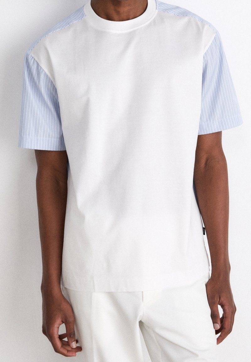 Lyhythihainen paita, jossa on valkoinen etuosa ja siniraidalliset hihat. Valmistettu pehmeästä kankaasta, jossa on pyöreä pääntie ja rento istuvuus.