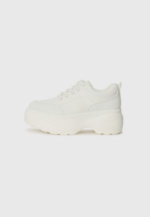 Sneaker bianca con suola in gomma spessa, materiale superiore liscio, design con lacci e dettagli di cucitura subtile sui lati.